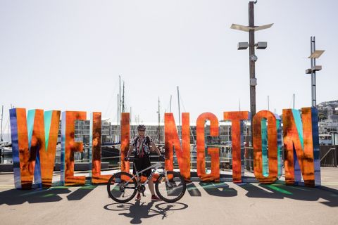 Cyclist standing infront of Wellington sign with a bike