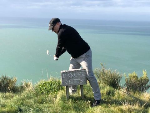 Jon taking a golf shot from a cliff edge in Napier