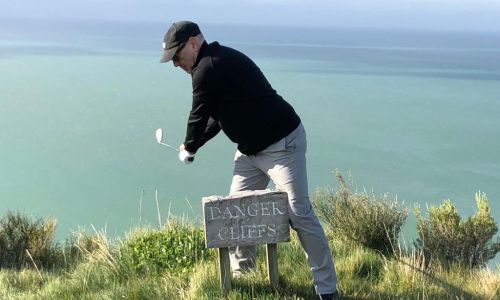 Jon taking a golf shot from a cliff edge in Napier